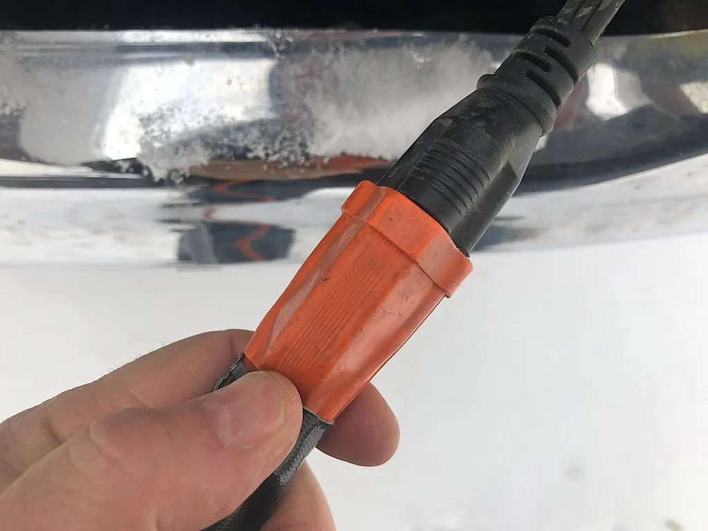 A block heater cord plug held in a hand on a cold winter morning
