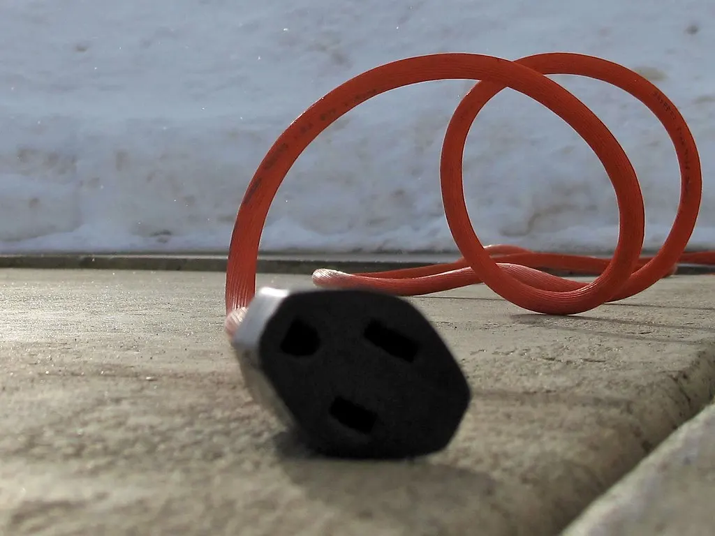 An orange extension cord running to a block heater through fresh snow